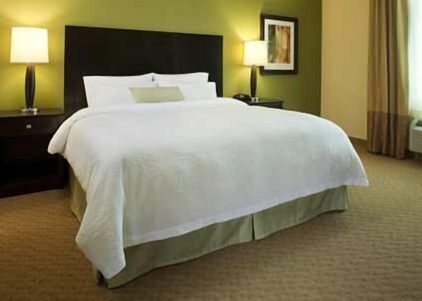 A neatly made bed with white linens in a hotel room with green walls, a dark headboard, and two bedside lamps.