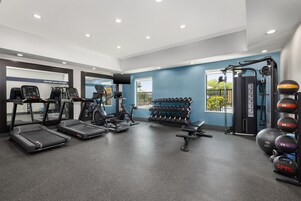 Un gimnasio con cintas de correr, elípticas, un banco de pesas, mancuernas y una máquina de poleas.