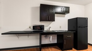 A compact kitchen with a black countertop, a microwave, a sink, and a black refrigerator. - Motel 6 Wilkes Barre, PA - Arena (Wilkes-Barre)