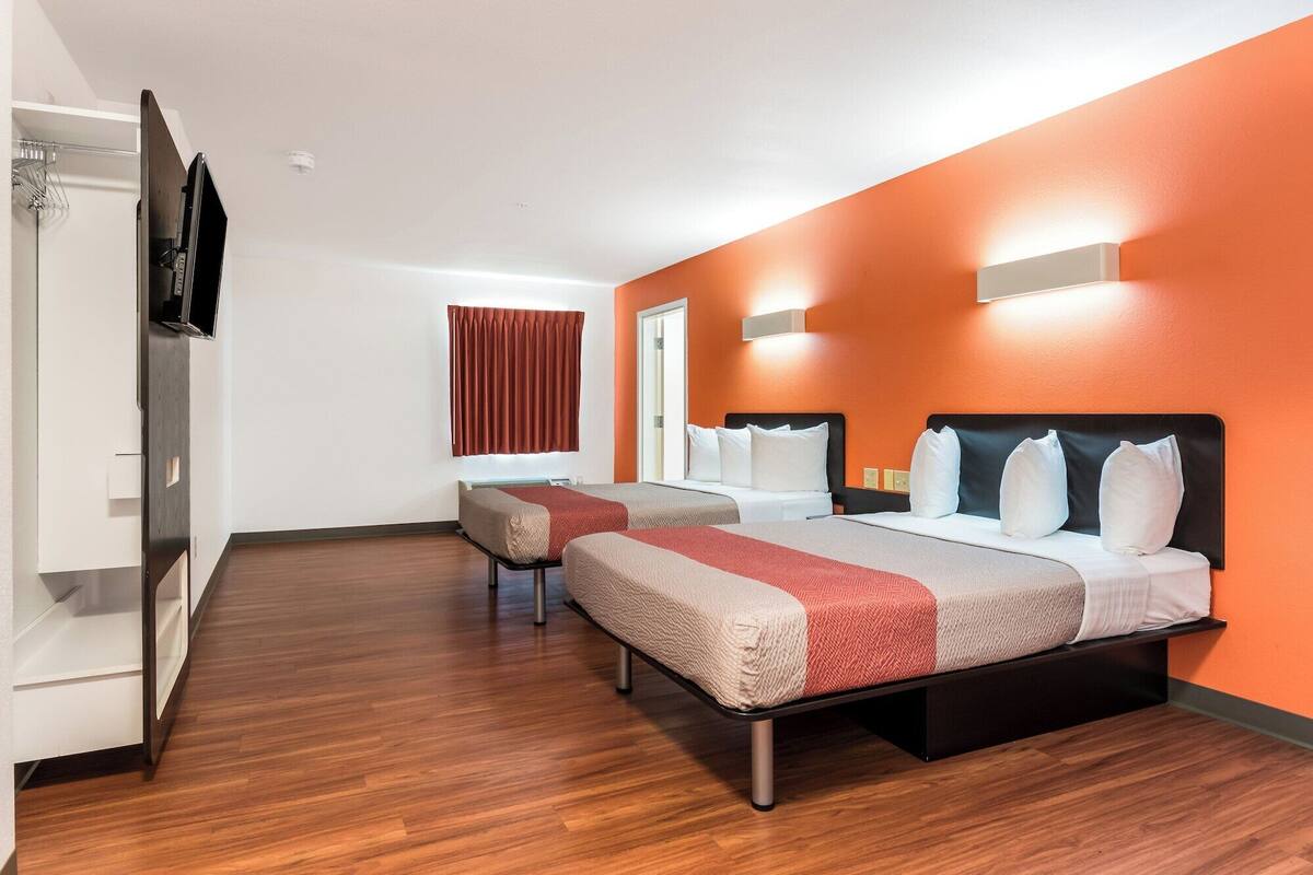 Une chambre d’hôtel avec deux lits, une armoire, une télévision et une fenêtre avec des rideaux.