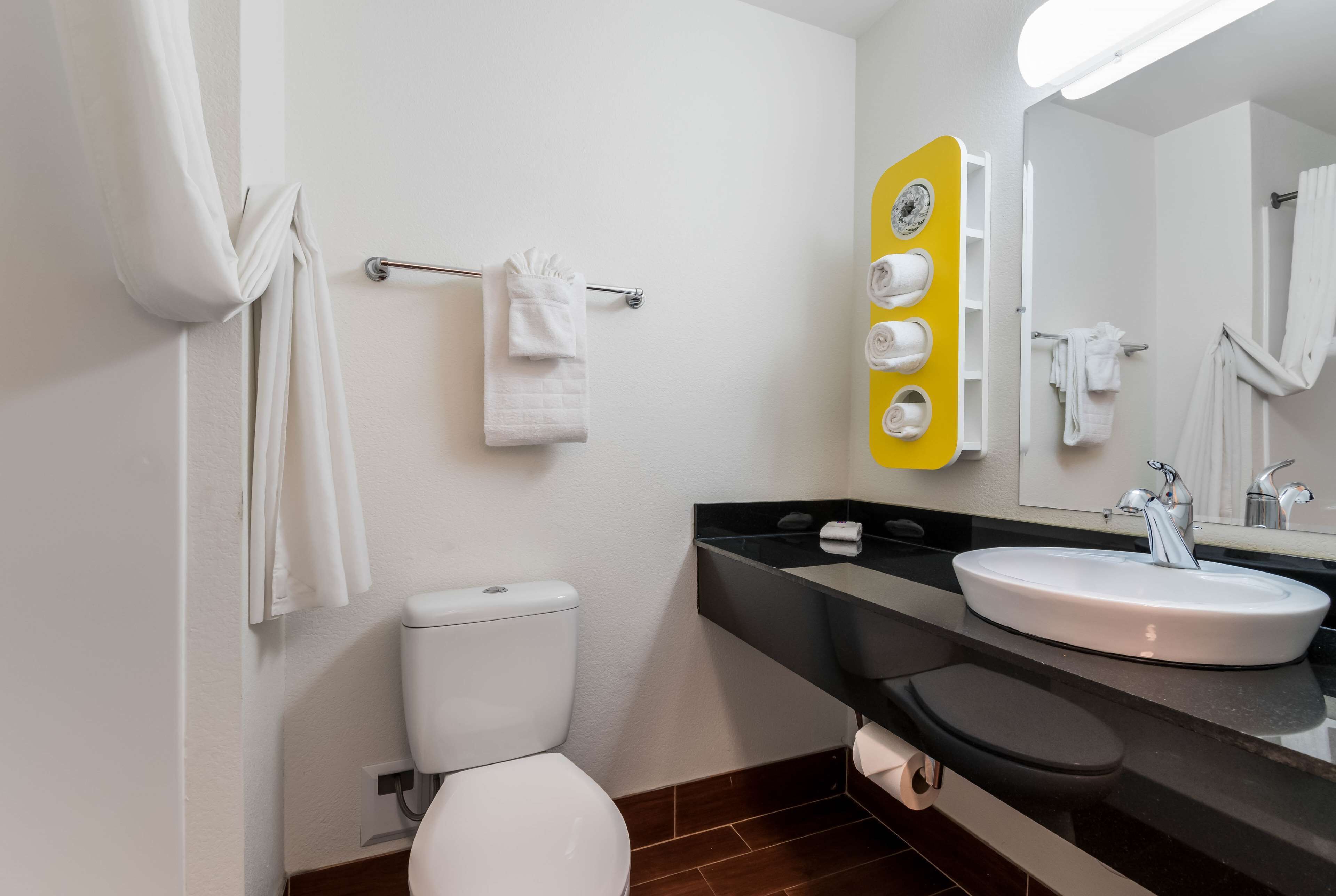 A bathroom with a white toilet, a black sink, and a mirror with a yellow towel rack.