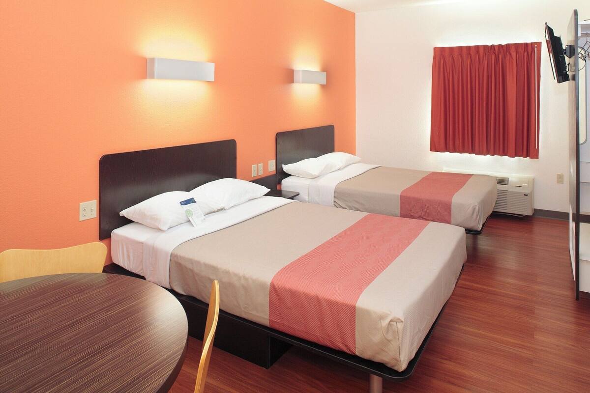 Une chambre d’hôtel avec deux lits, une table ronde et un téléviseur fixé au mur.