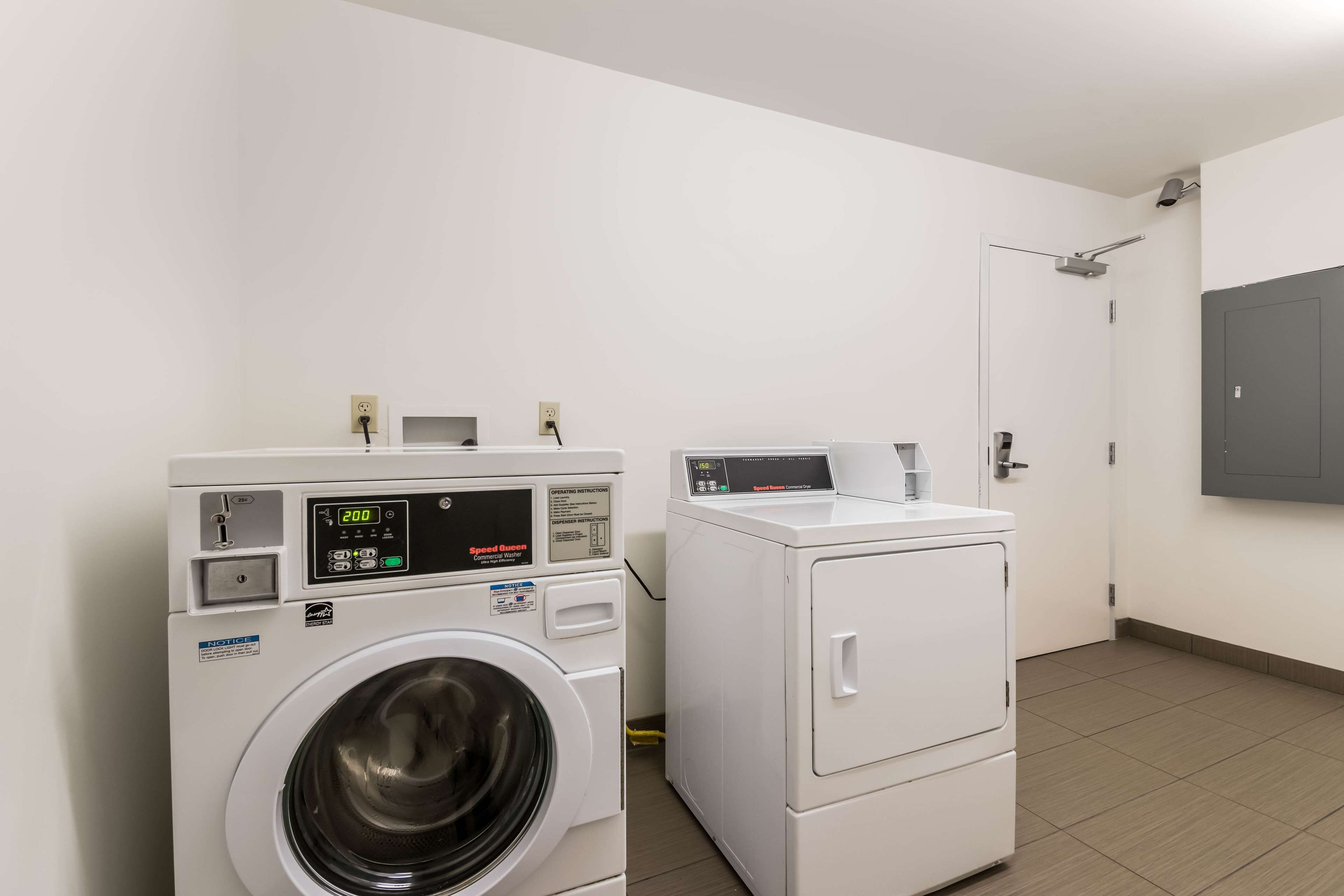 Una sala de lavandería con lavadora y secadora de carga frontal, una puerta y un panel eléctrico fijado a la pared.