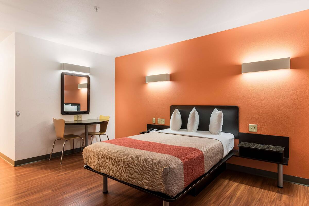 Une chambre d’hôtel équipée d’un lit, d’un bureau, d’une chaise et de deux lampes fixées au mur.