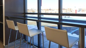 A seating area with three chairs and a table, large windows with a view of a parking lot and buildings. - Motel 6 Wilkes Barre, PA - Arena (Wilkes-Barre)