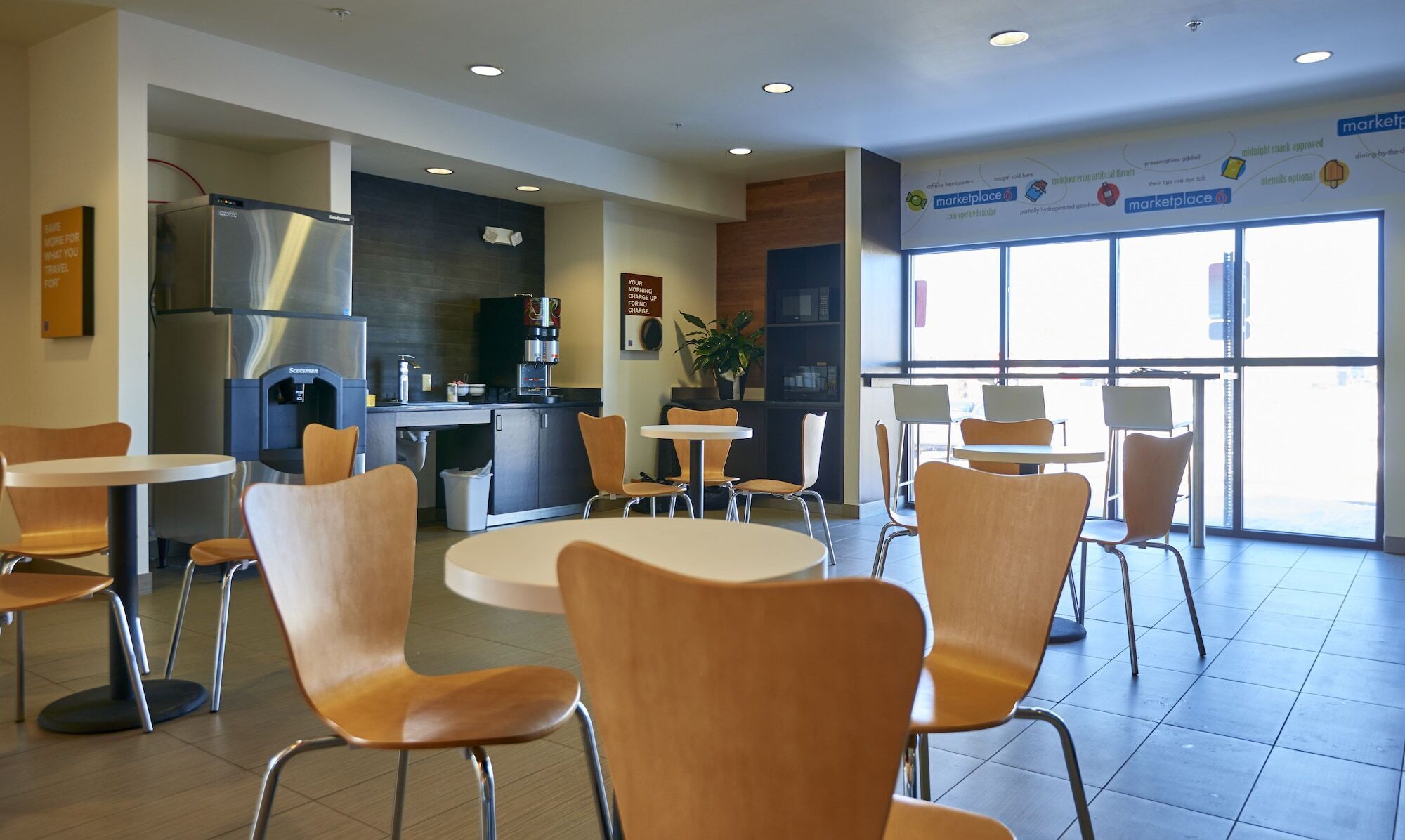 A modern cafe with round tables and wooden chairs, a coffee machine, and a large window offering a view.