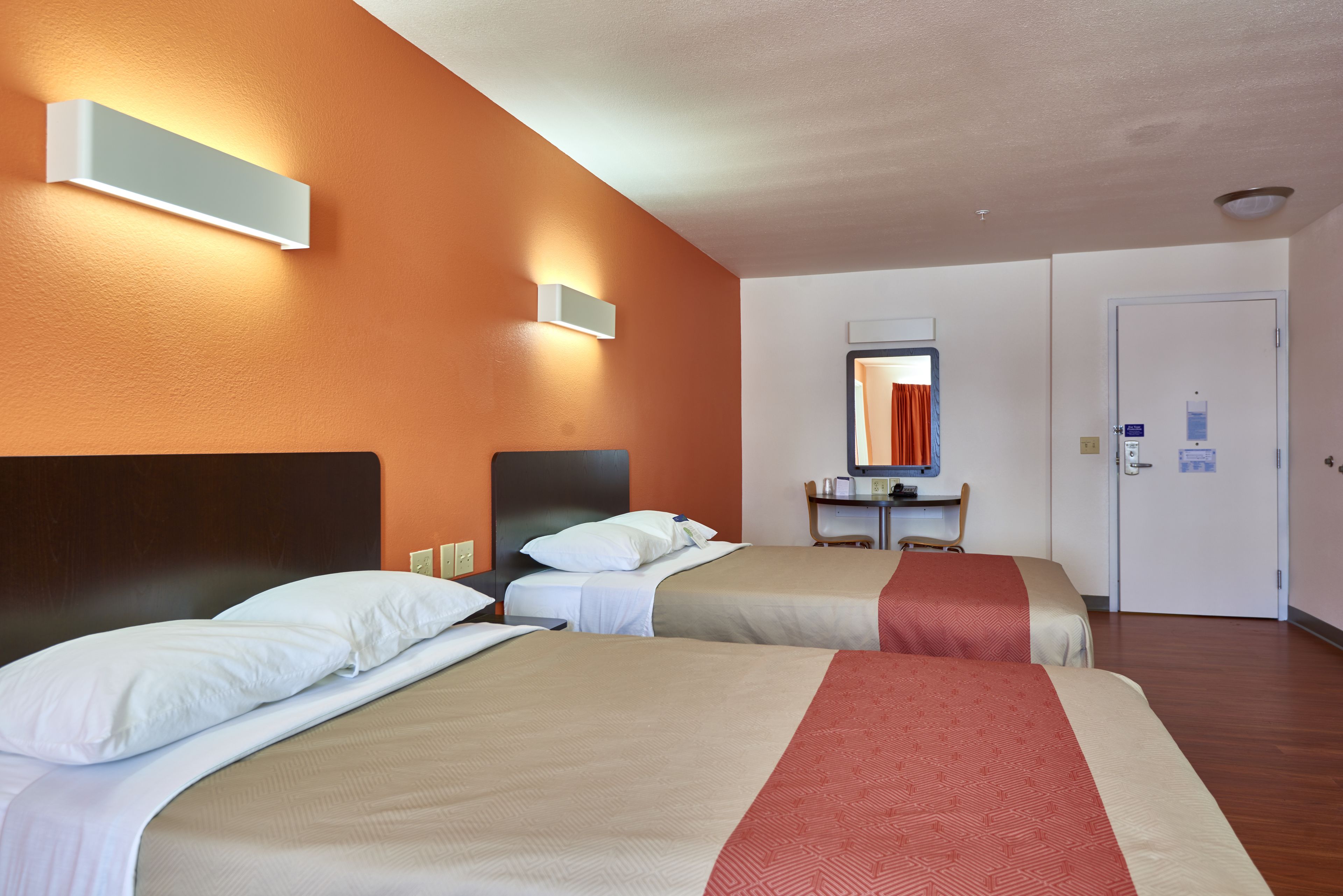 Una habitación de hotel con dos camas, un escritorio pequeño, un espejo y una puerta.