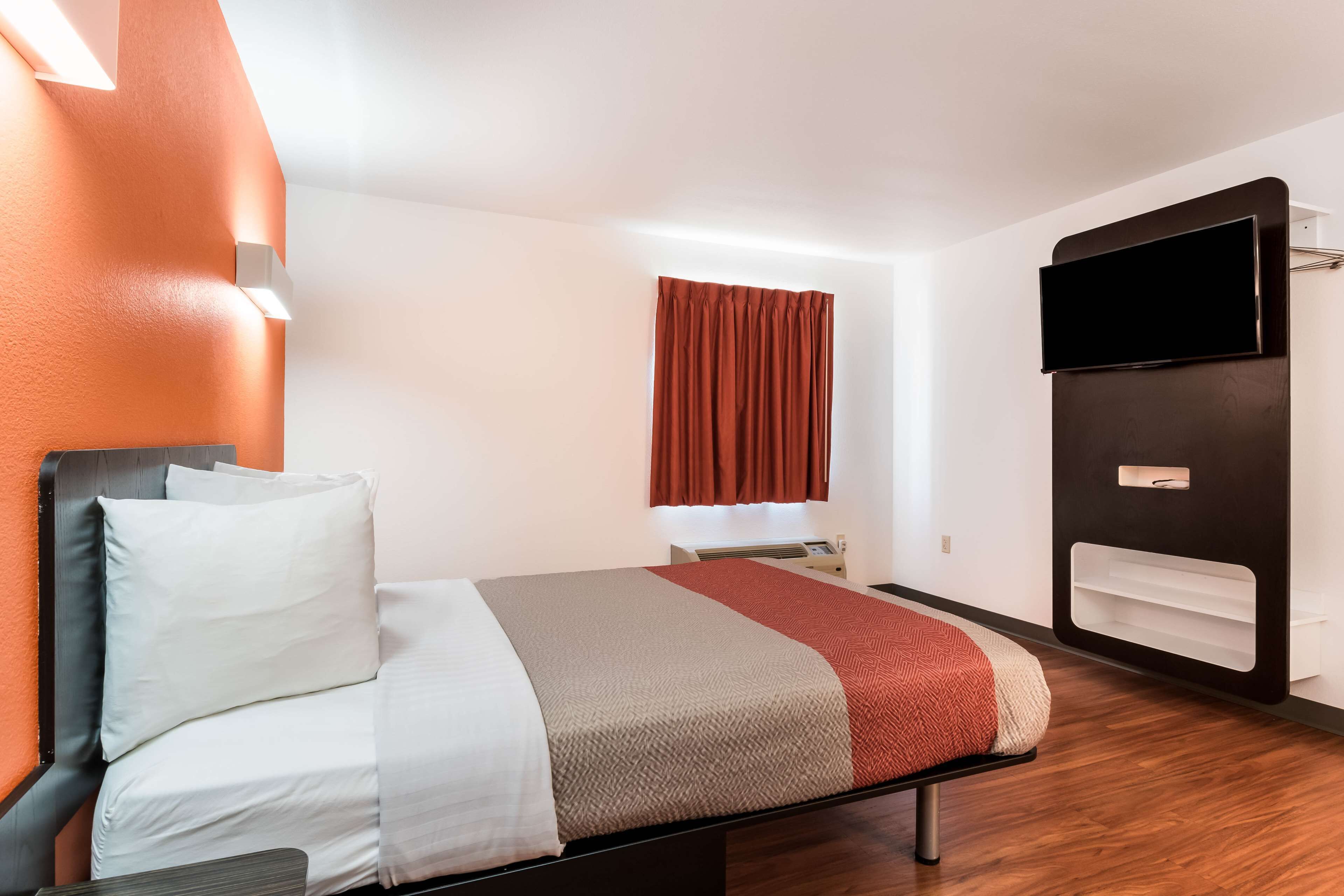 Una habitación de hotel moderna con una cama, un televisor de pantalla plana, una ventana con cortinas y un estante empotrado.