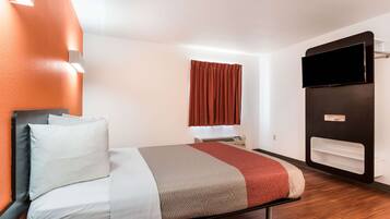 Una habitación de hotel moderna con una cama, un televisor de pantalla plana, una ventana con cortinas y un estante empotrado.