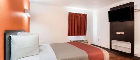 A modern hotel room with a bed, a flat-screen TV, a window with curtains, and a built-in shelf.