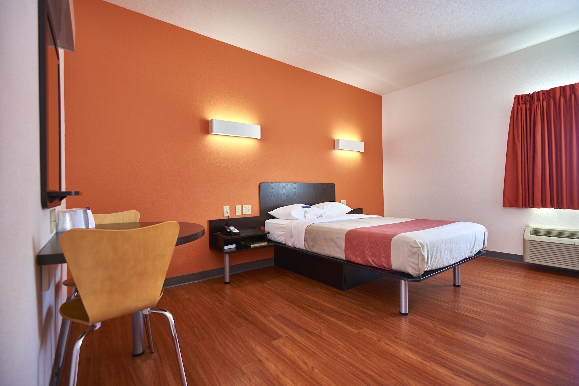 A hotel room with a bed, a desk with a chair, a nightstand, and two wall-mounted lights.