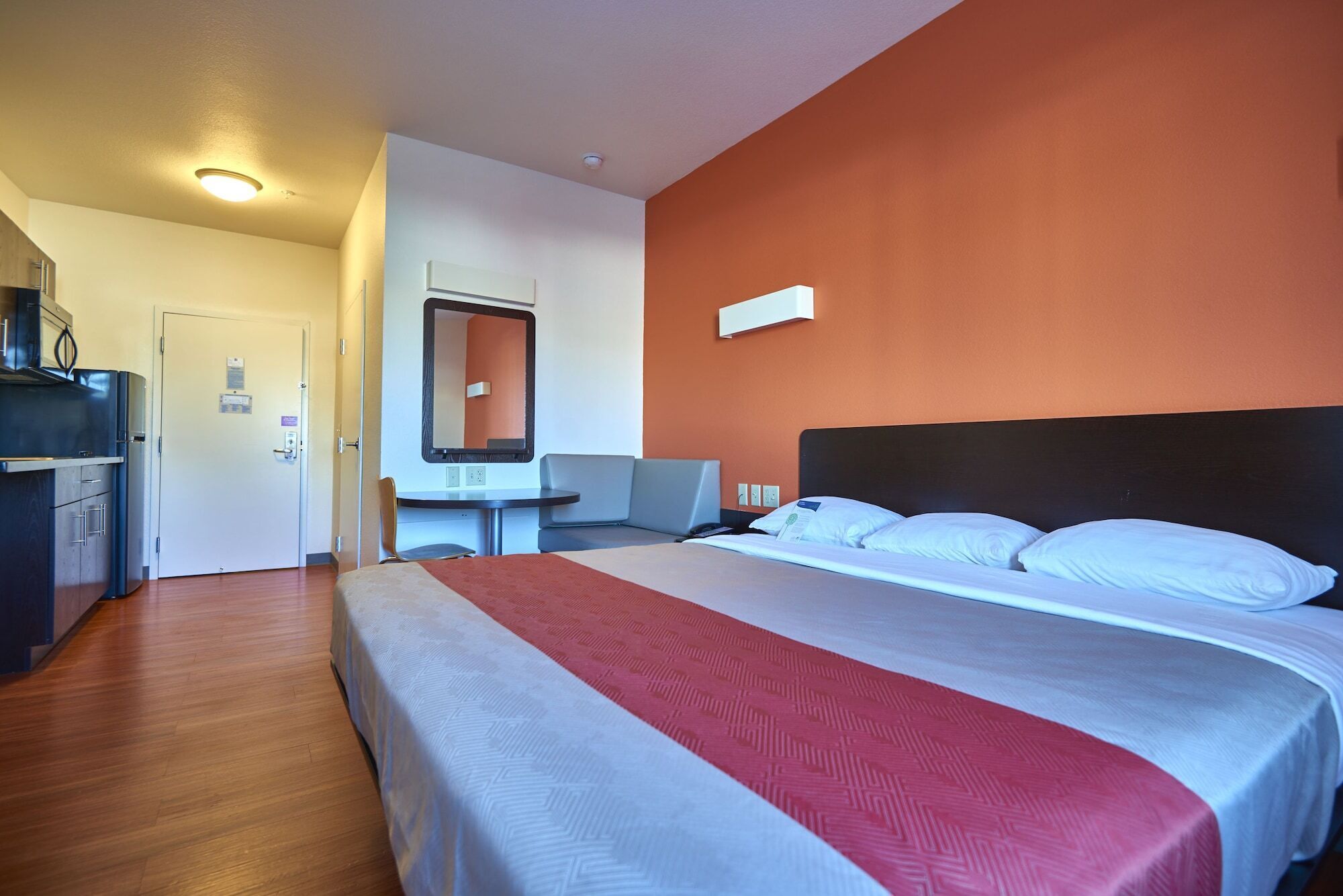 A hotel room with a bed, a desk, a chair, and a kitchenette.