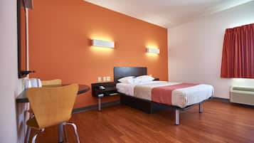 A hotel room with a bed, a chair, a desk, and a wall-mounted air conditioner.