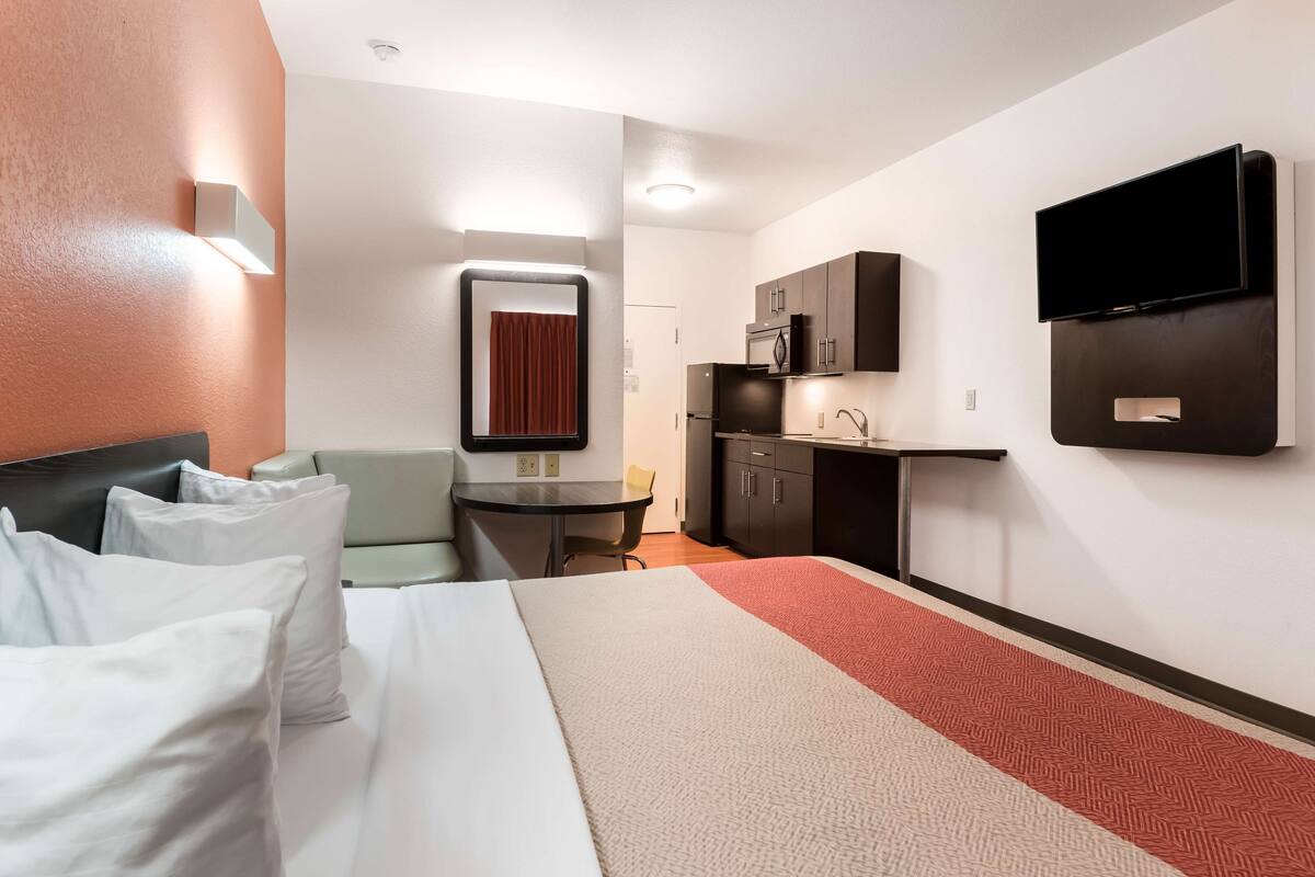 Une chambre d’hôtel équipée d’un lit, d’un bureau, d’une chaise, d’un four à micro-ondes, d’une télévision et d’une petite kitchenette.