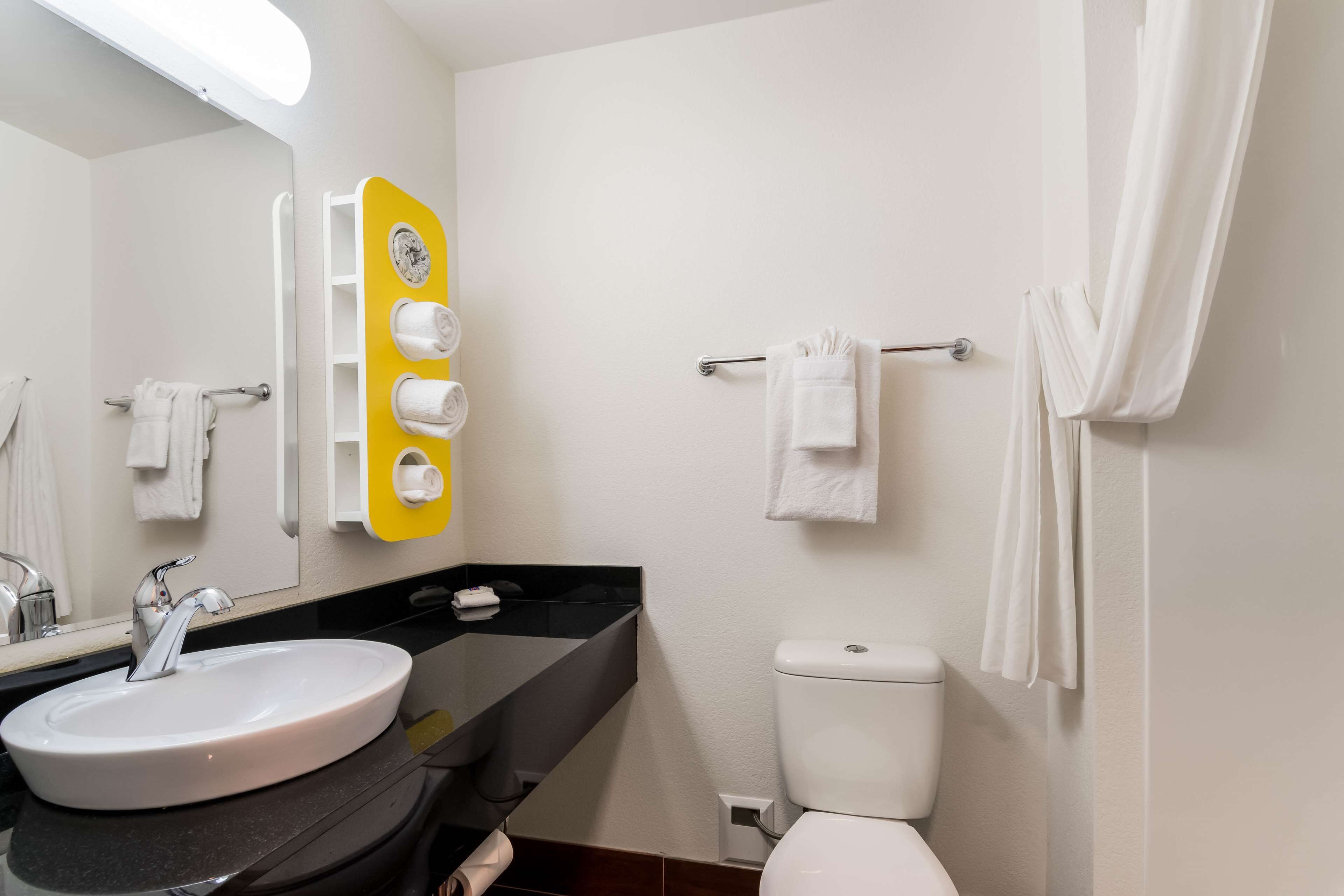 A modern bathroom with a white sink, a mirror, a toilet, and a towel rack.