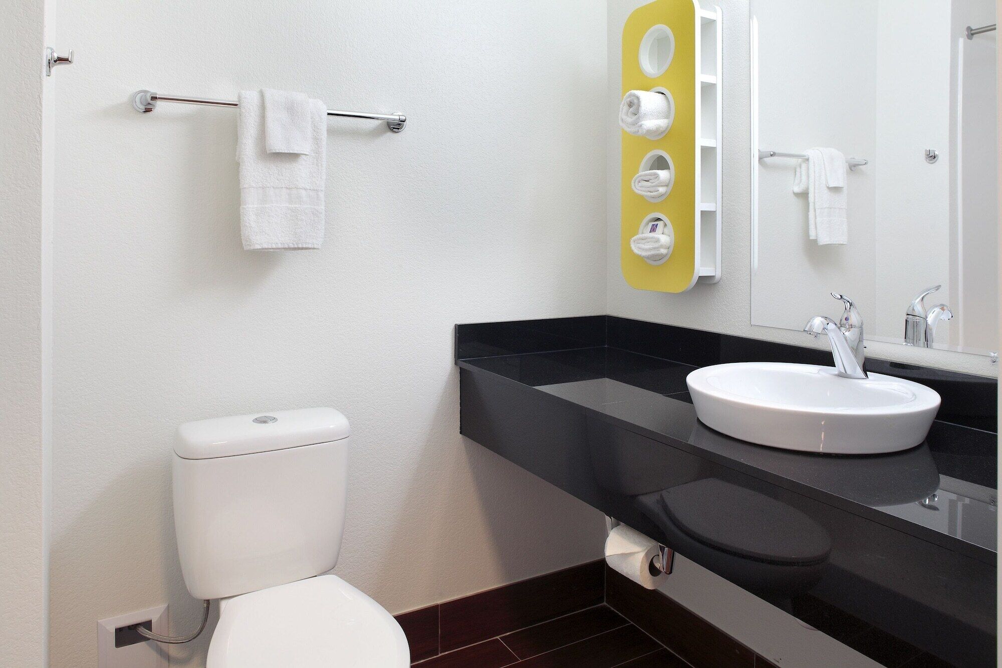 Un baño moderno con inodoro blanco, lavamanos negro y espejo con detalle amarillo.