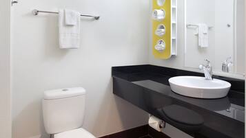 Un baño moderno con inodoro blanco, lavamanos negro y espejo con detalle amarillo.