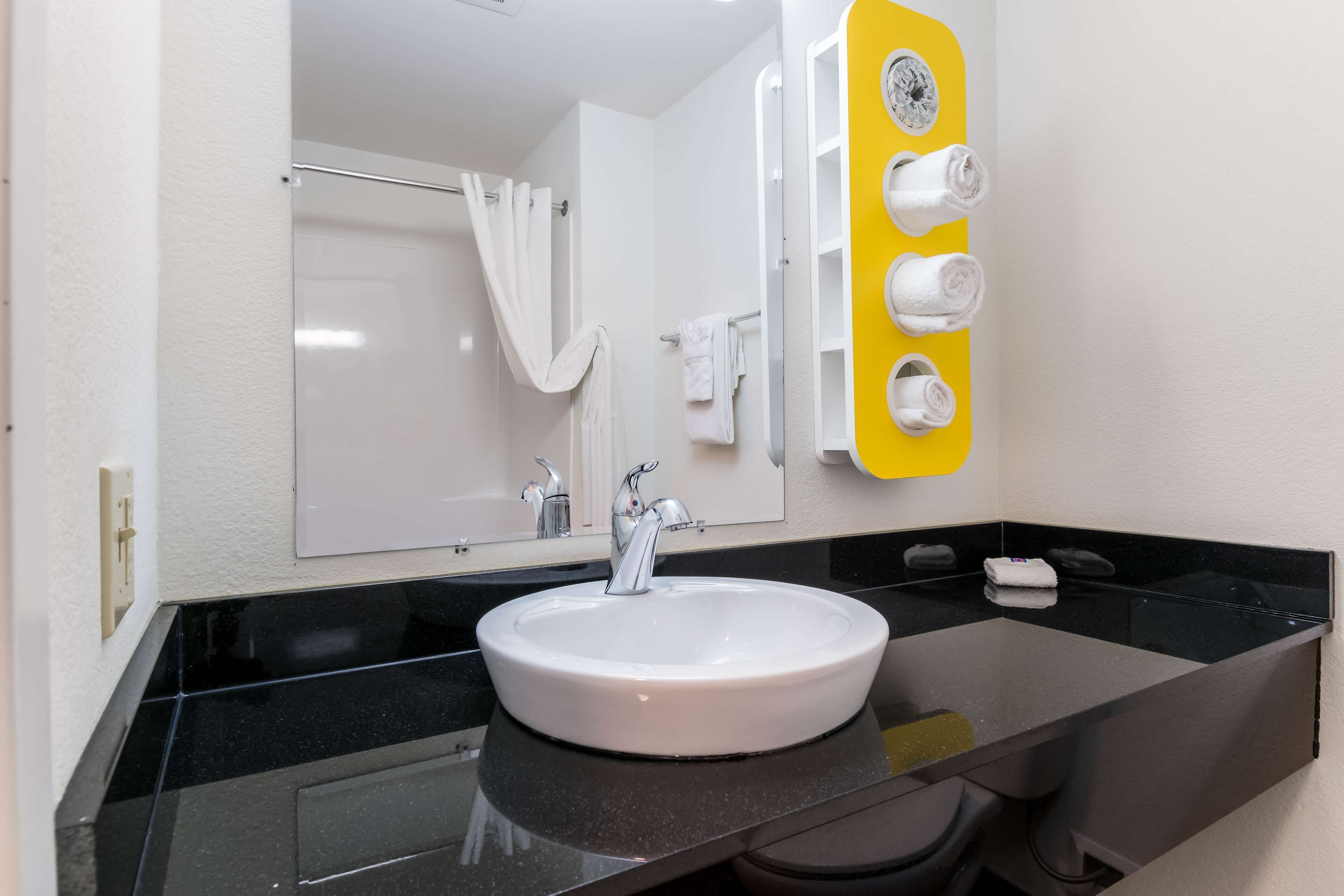A bathroom with a white sink, black countertop, and a mirror with a yellow towel rack.