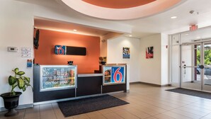 A hotel reception area with a modern design, featuring a reception desk, a digital thermostat, and a potted plant. - Motel 6 Wilkes Barre, PA - Arena (Wilkes-Barre)