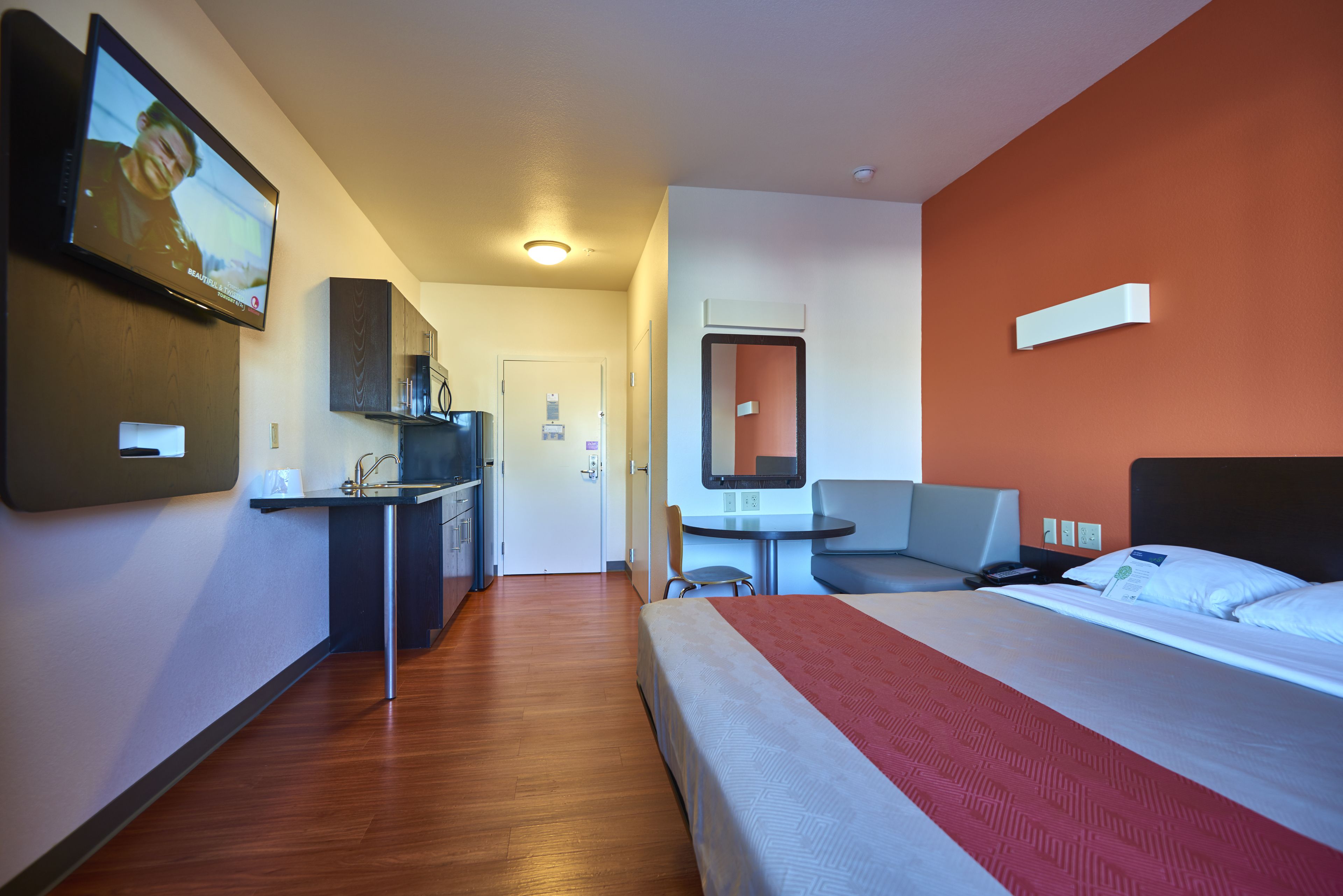 A hotel room with a bed, a desk with a chair, a small table, and a TV mounted on the wall.