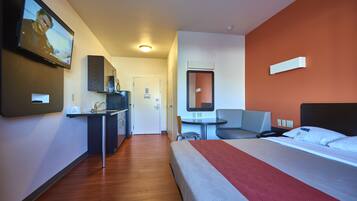 A hotel room with a bed, a desk with a chair, a small table, and a TV mounted on the wall.