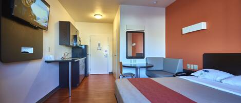 A hotel room with a bed, a desk with a chair, a small table, and a TV mounted on the wall.