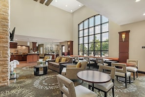 A spacious lobby with a seating area, a bar, and a kitchen in the background. - Staybridge Suites Plano North - Frisco by IHG (Plano)
