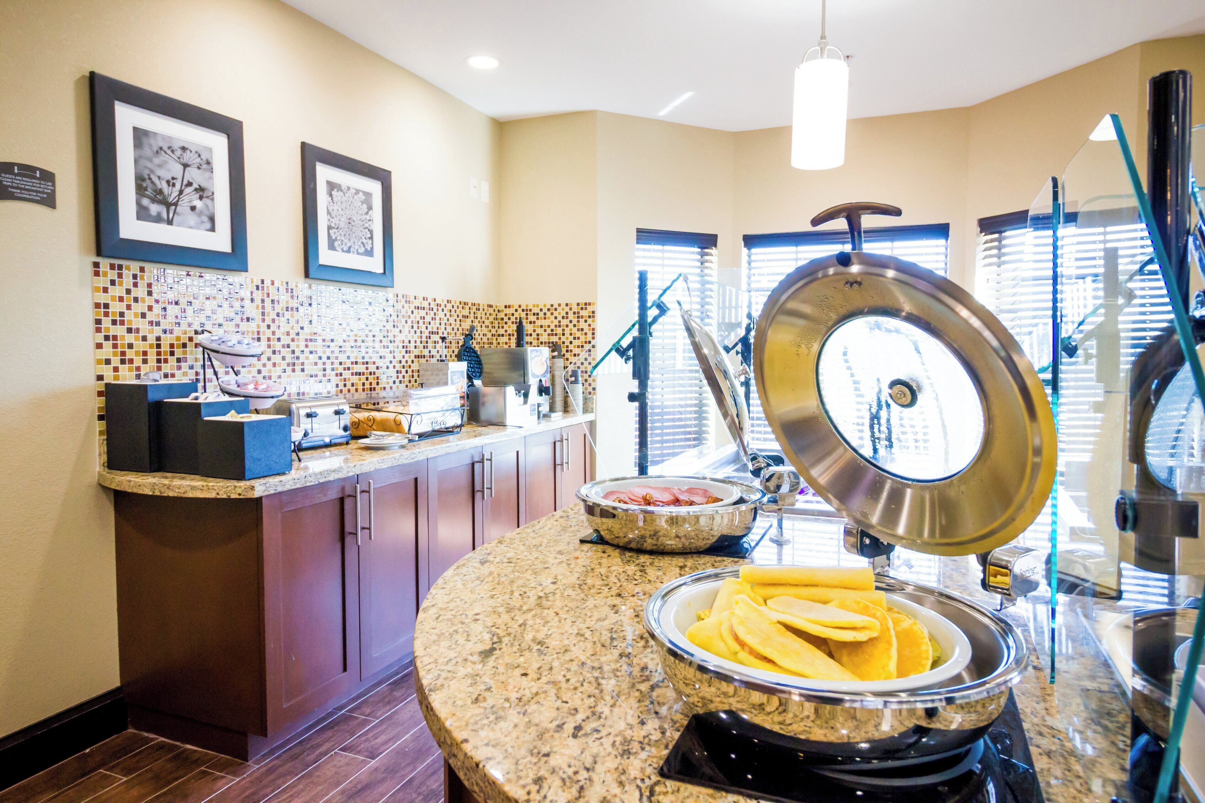 A kitchen with granite countertops, a buffet setup, and a window with blinds.