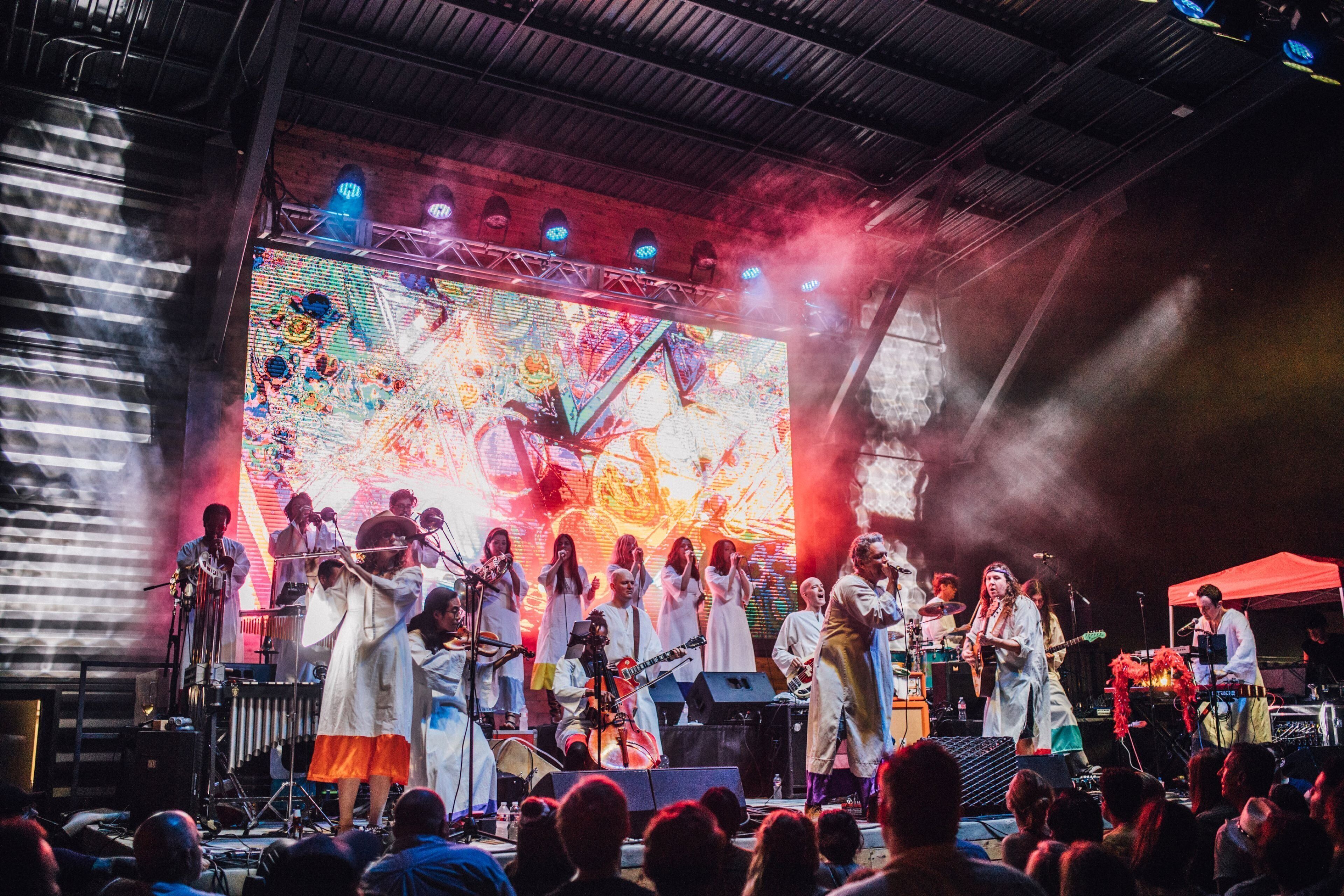 A band performing on a stage with a large screen displaying abstract visuals.