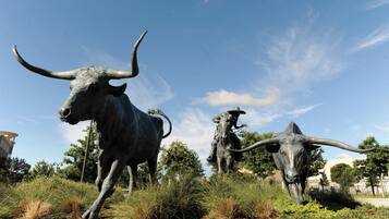 A sculpture of a bull and a cowboy in a grassy area with trees and a clear sky.
