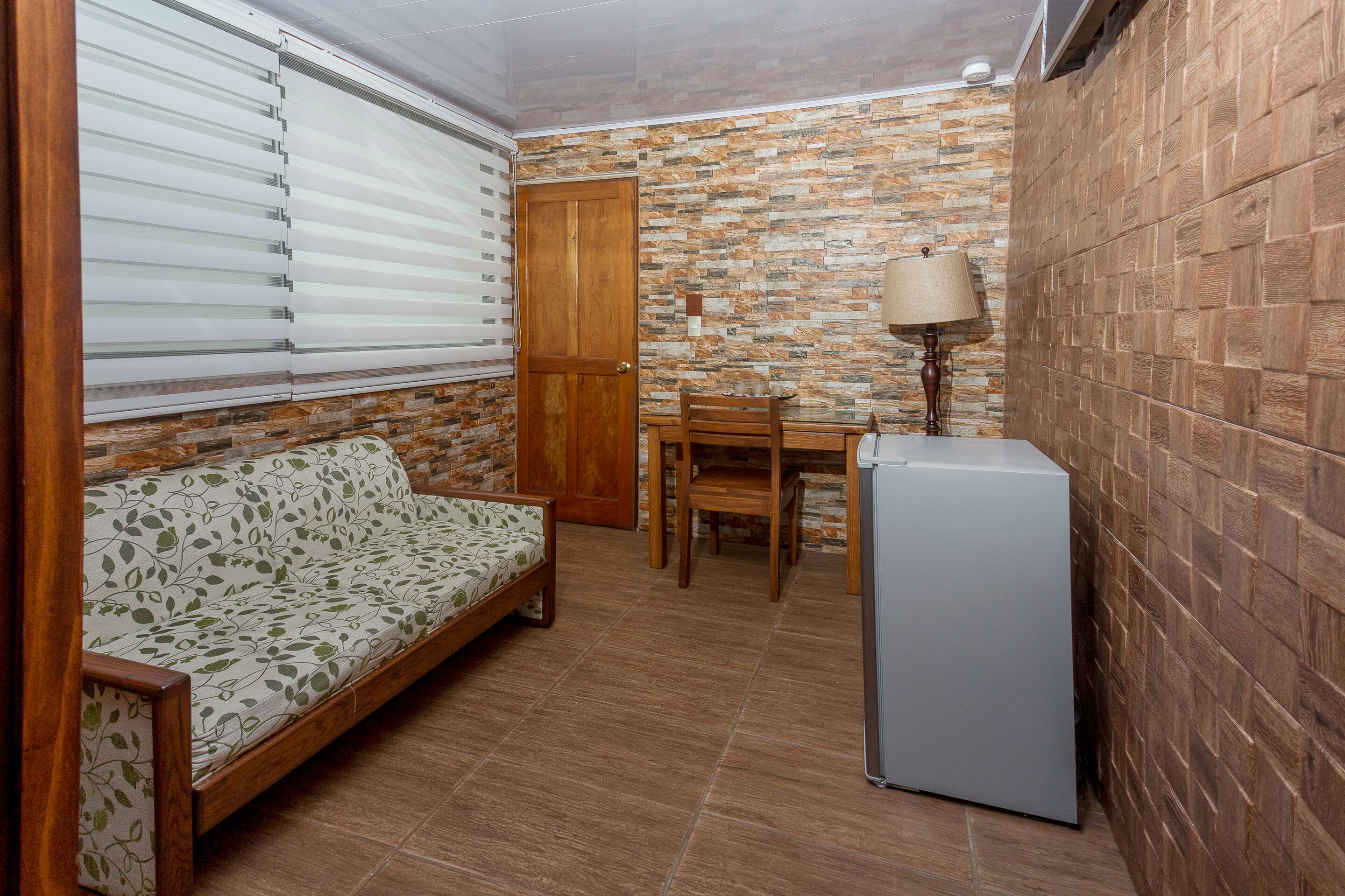 A compact room with a sofa, a wooden table, a chair, and a refrigerator.