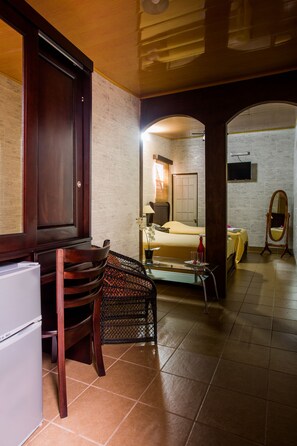 Une chambre d’hôtel de taille réduite, comprenant un lit, un bureau avec une chaise, une petite table, un miroir et un téléviseur fixé au mur.