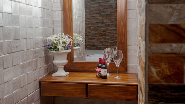 A wooden vanity with a mirror, a vase of flowers, and two wine bottles with glasses.