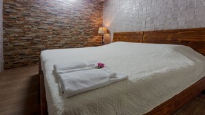 A neatly made bed with a white quilt and folded towels, a wooden headboard, a stone-patterned wall, and a lamp on a nightstand.