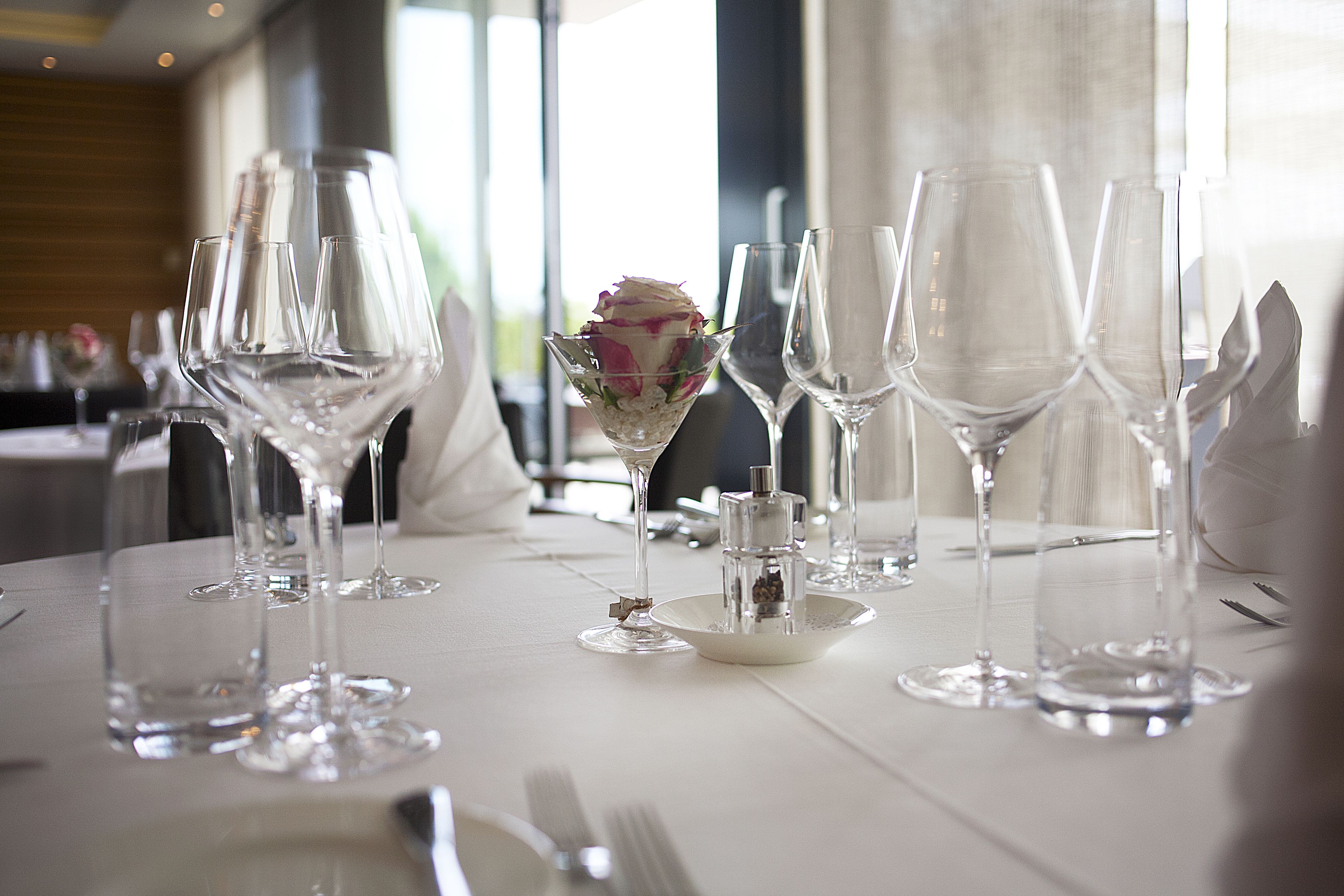 Mesa dispuesta para una ocasión de cena formal, con varias copas de vino y un centro de mesa con una rosa blanca en un cuenco de vidrio.