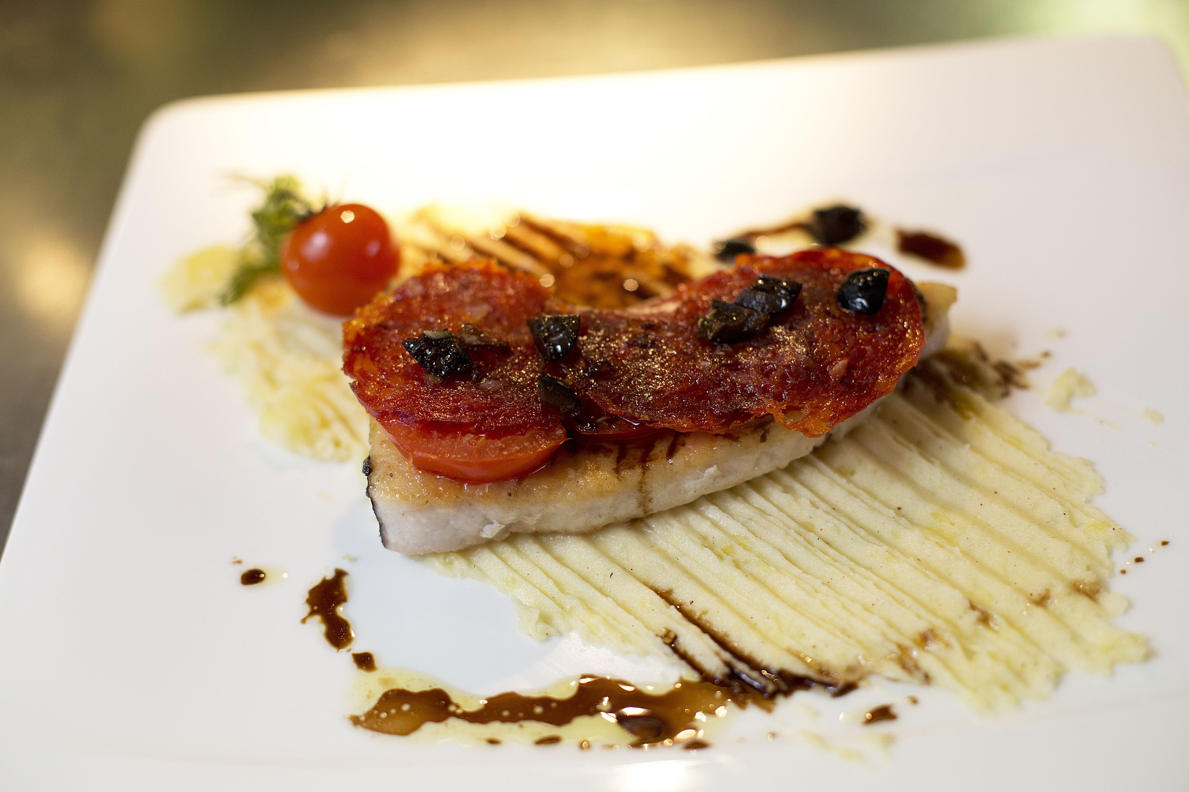 Un plato con una rebanada de carne, un tomate cherry y un chorrito de salsa.
