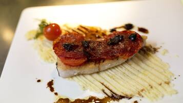 Un plato con una rebanada de carne, un tomate cherry y un chorrito de salsa.