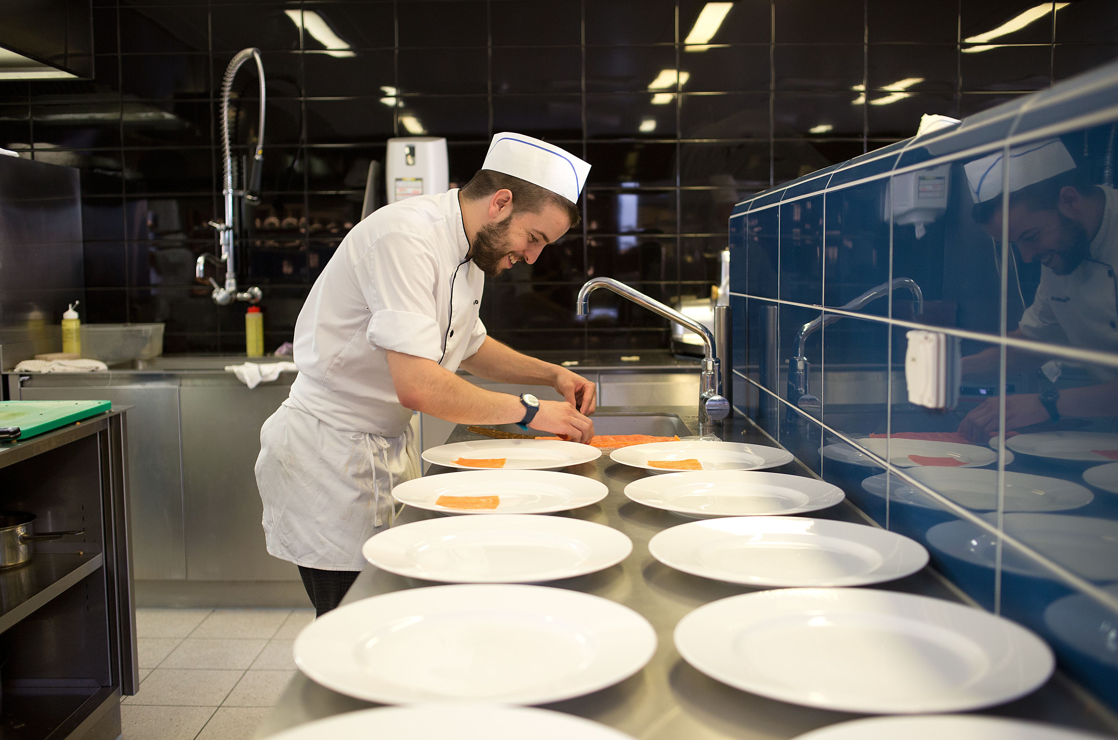 Un chef prepara alimentos en una cocina profesional con superficies de acero inoxidable y varias fuentes.