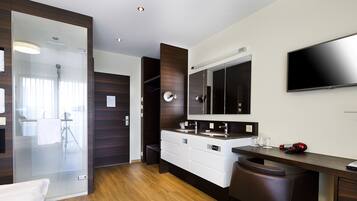 Un baño moderno con cabina de ducha de vidrio, un espejo grande y un tocador con televisor de pantalla plana.