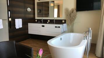 Une salle de bain moderne avec une baignoire sur pieds, un grand miroir et un téléviseur à écran plat fixé au mur.