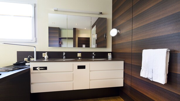 A modern bathroom with a wooden vanity, a large mirror, and a towel hanging on the wall. - Hôtel Glanis (Gland)
