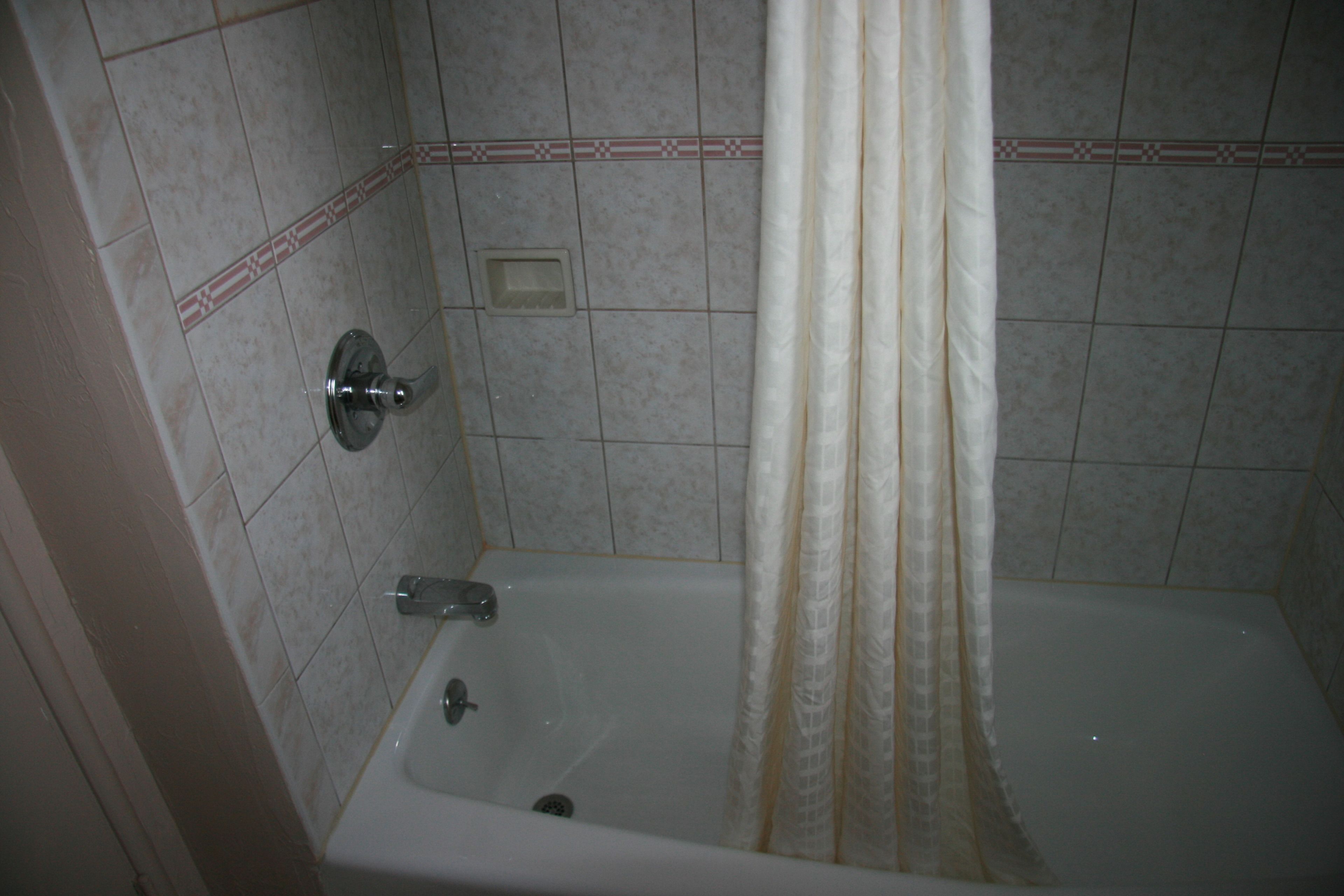 A bathroom with a bathtub, shower curtain, and tiled walls.