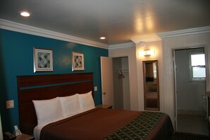A hotel room with a large bed, a wooden headboard, teal walls, and a door leading to a bathroom. - Civic Center Lodge (Oakland)