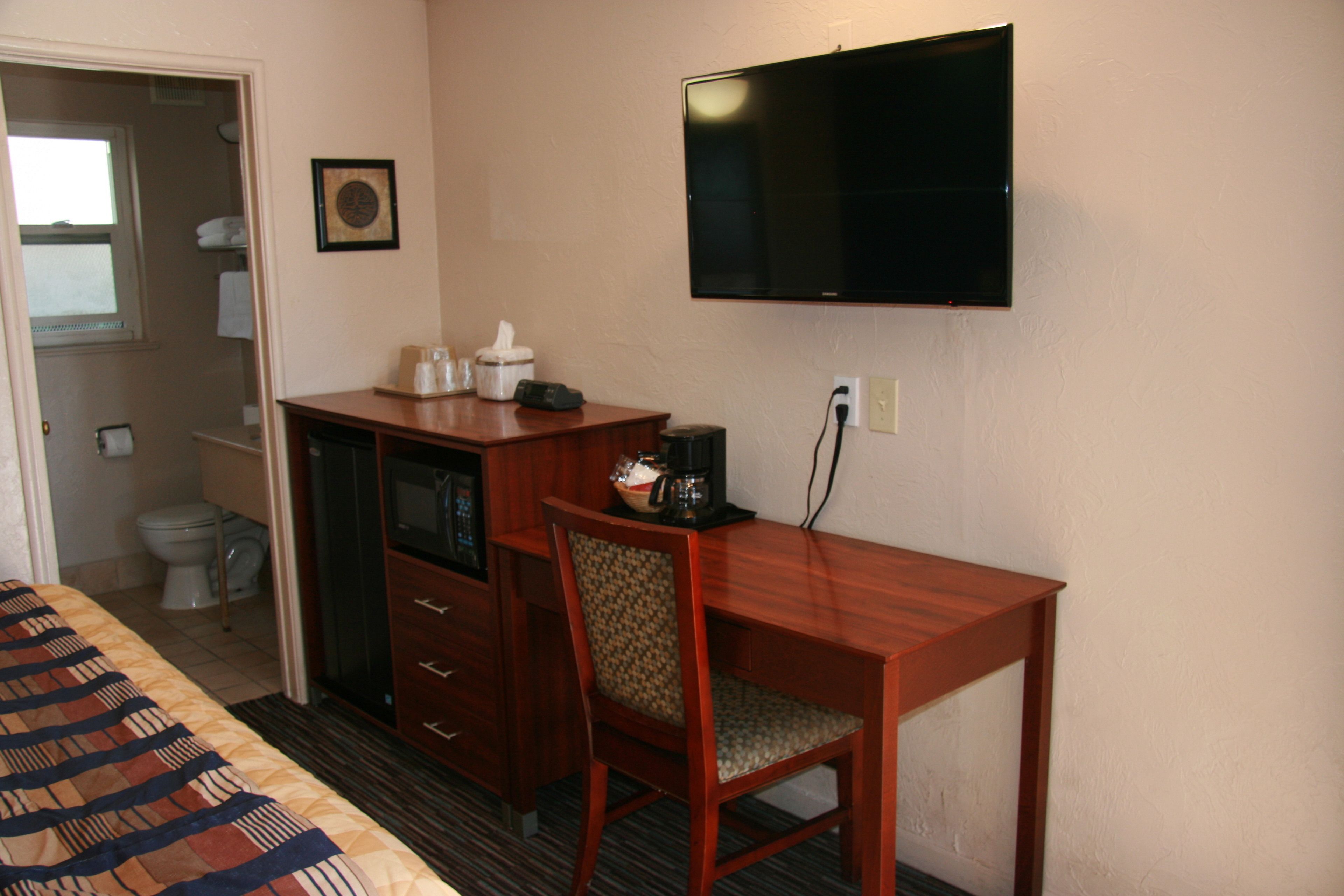 Una habitación de hotel con cama, escritorio, silla, televisor y baño.