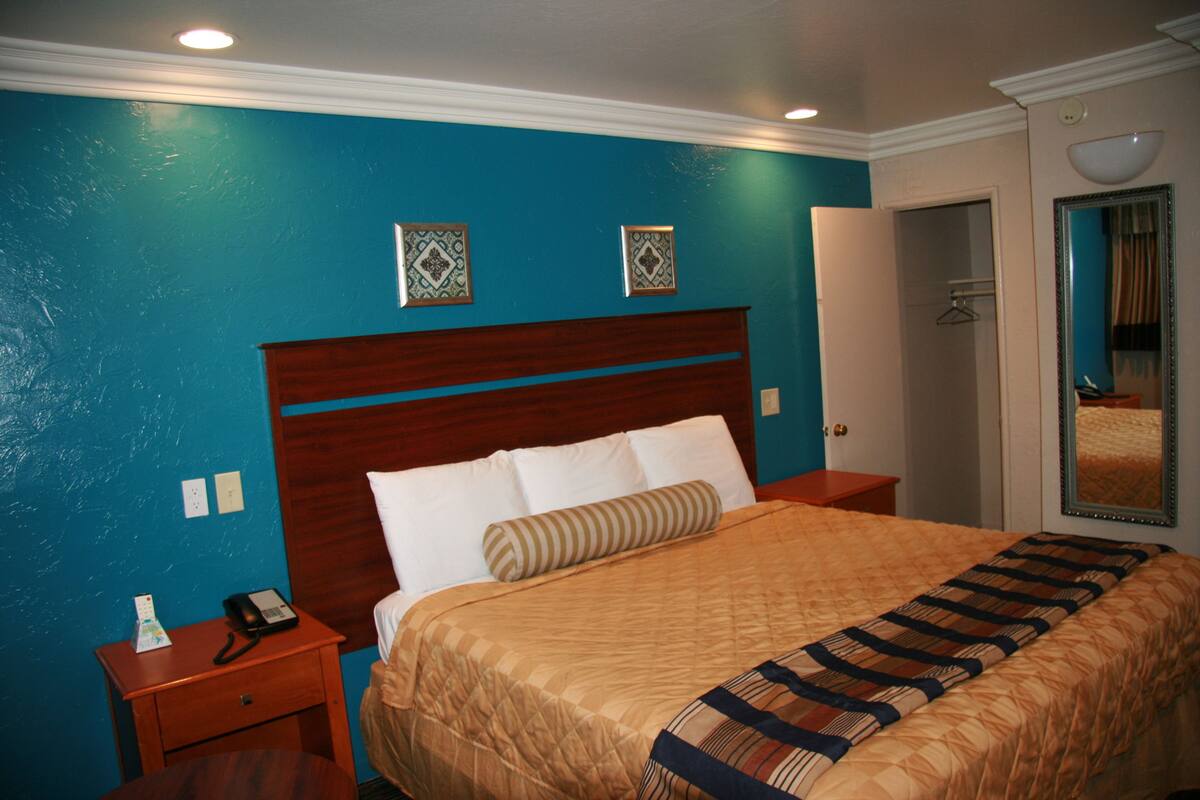 A hotel room with a large bed, wooden headboard, and a blue accent wall.