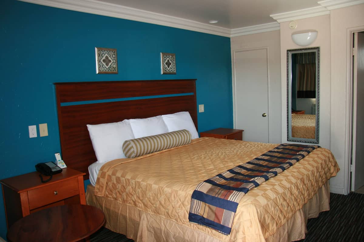 A hotel room with a large bed, a wooden headboard, a bedside table with a phone, and a mirror on the wall.