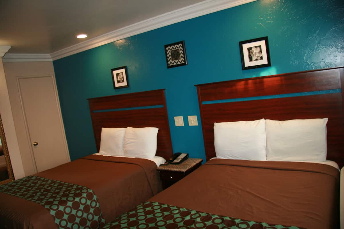 A hotel room with two beds, teal walls, and wooden headboards.