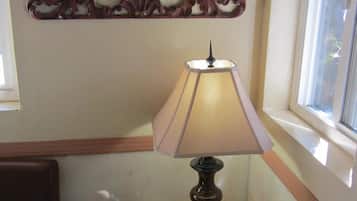 A corner with a lamp on a small table, a decorative wall piece above the lamp, and a window with a view outside.