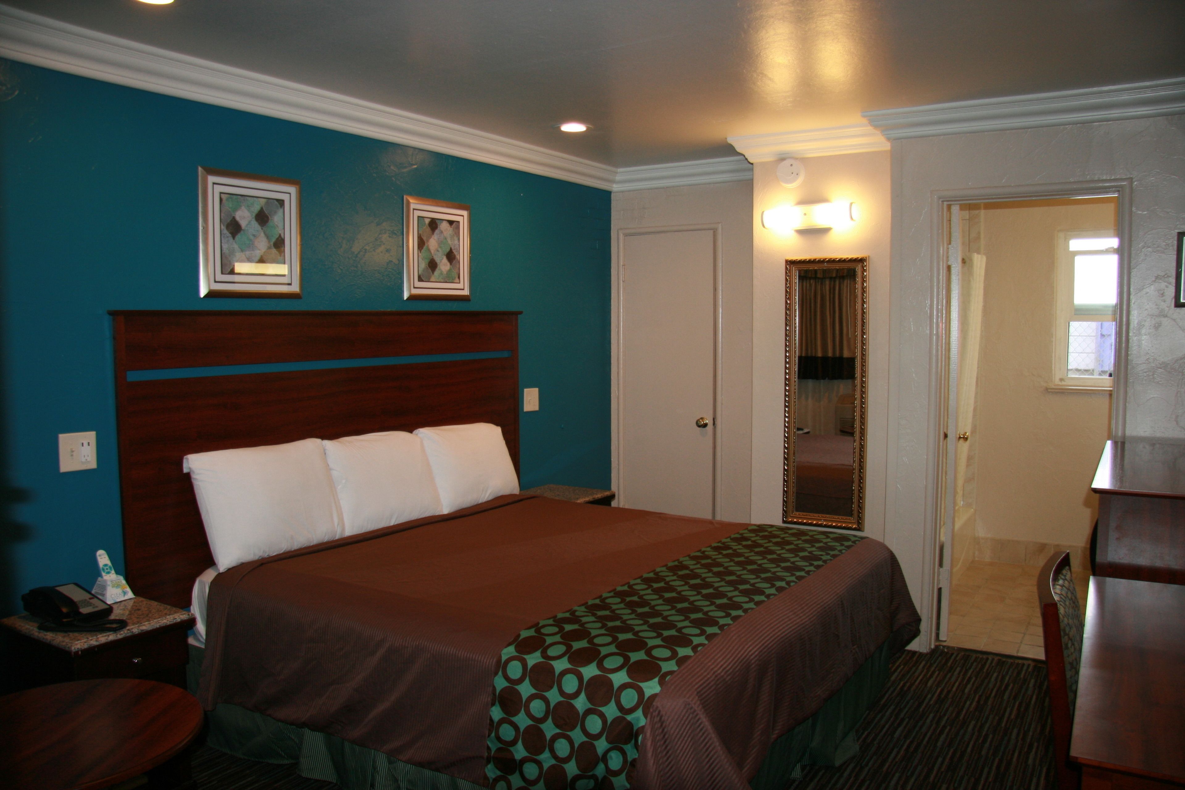 A hotel room with a large bed, a nightstand, a desk, and a door leading to a bathroom.