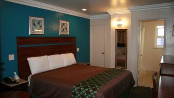 A hotel room with a large bed, a nightstand, a desk, and a door leading to a bathroom.